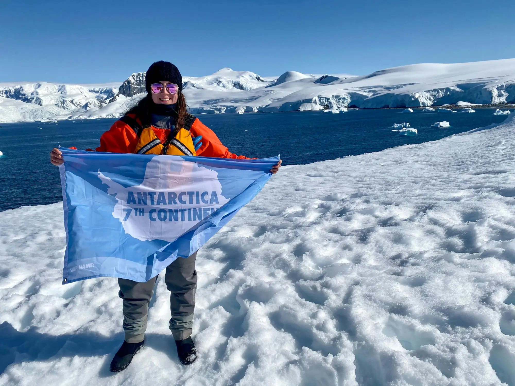 An explorer holding up the flag of Antarctica in Antarctica.