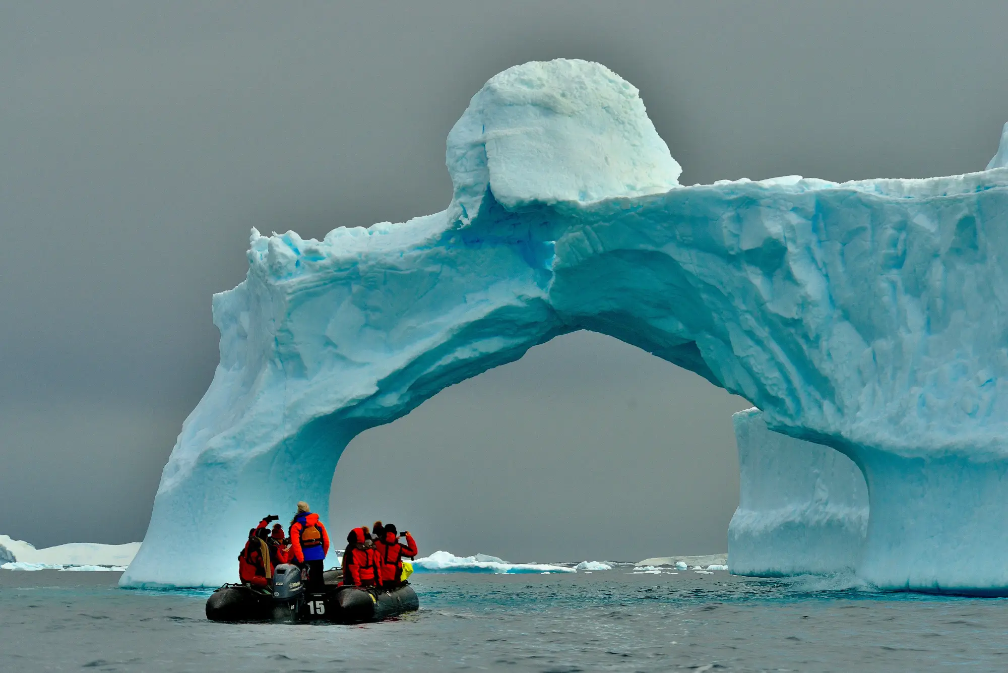 Explorers on a raft sailing under huge glaciers in Antarctica.